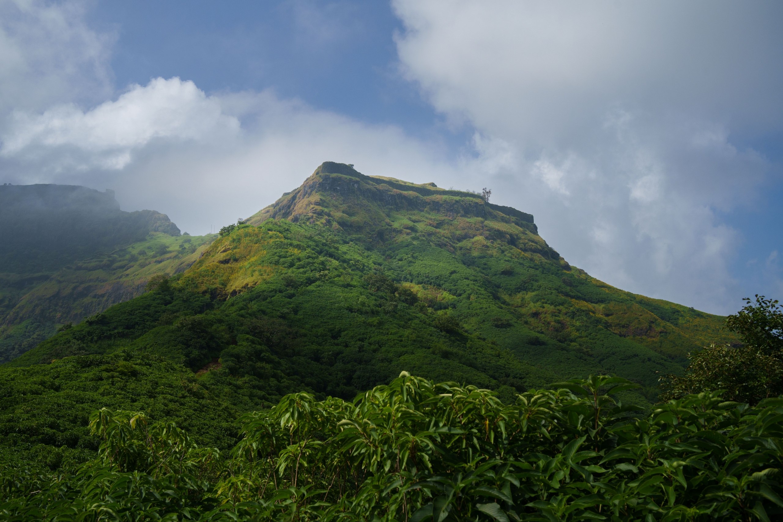 Looking up at the Tikona summit block against a monsoon sky, minutes before the final flight of steps.
