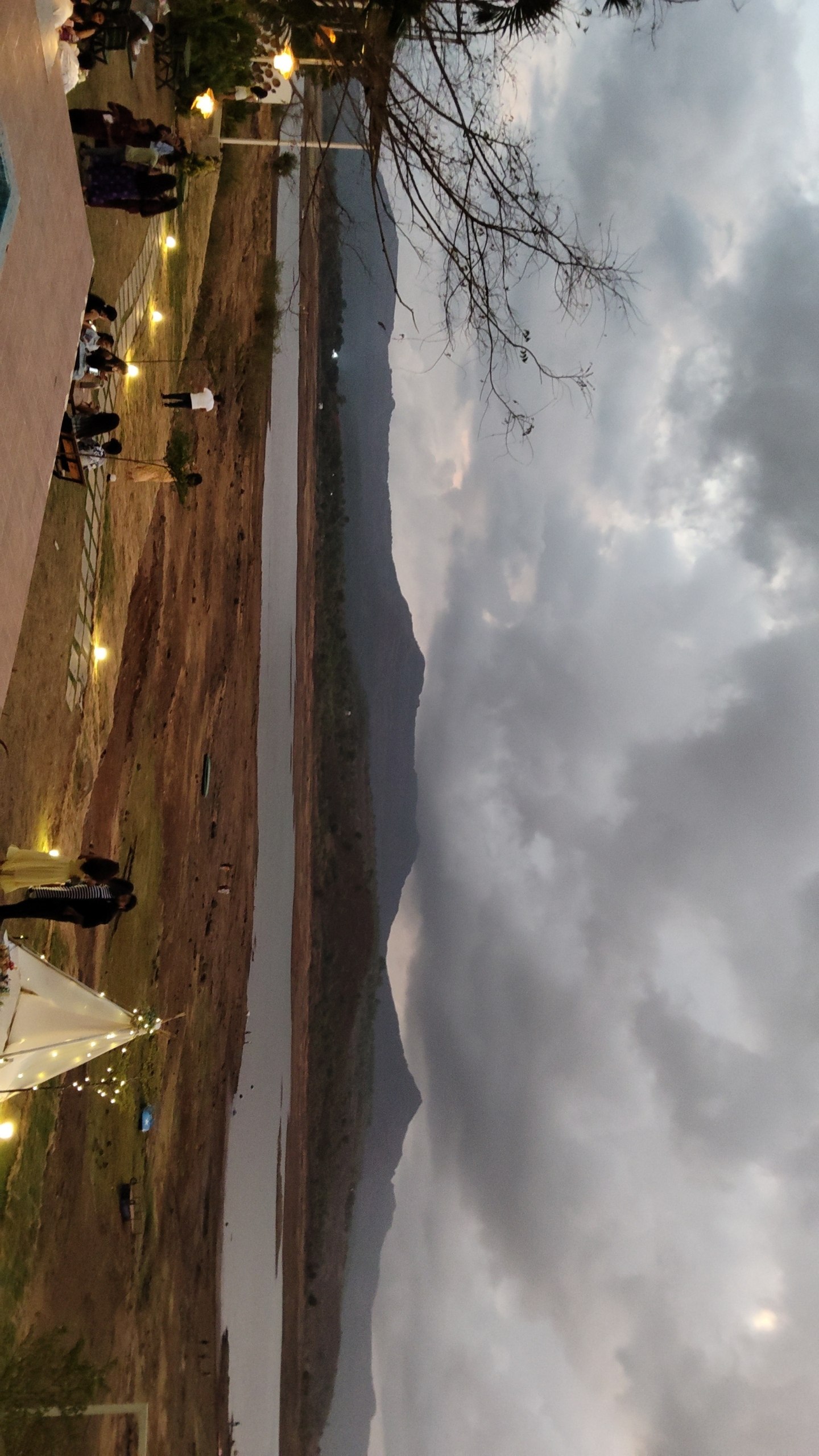 Blue hour on the Pawna shore — lit tents, still water and the bonfire being started behind us.